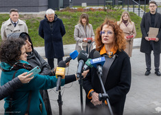 Kobieta przemawia, kilkanaście słucha, w tle widok bloków mieszkaniowych