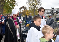 Ksiądz i ministranci idą alejka cmentarza