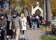 Kilkadziesiąt osób idzie alejką cmentarza