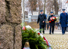 Mundurowi niosą kwiaty przed pomnik