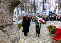 Kobieta i mężczyzna niosłą wieniec z biało-czerwonych kwiatów