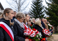 Grupa osób z biało-czerwpnymi wiązankami