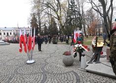 Ludzie zgromadzeni na placu.Na pierwszym planie bialo-czerwone flagi i wieńce