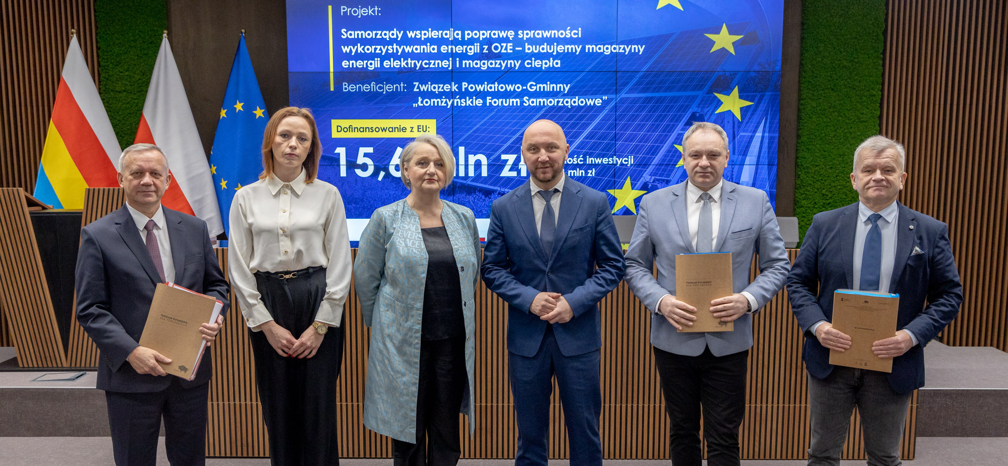 Sześć osób stoi na zdjęciu grupowym na tle telebimu