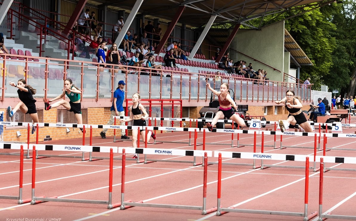 Zawodniczki biegną przez płotki na stadionie lekkoatletycznym.