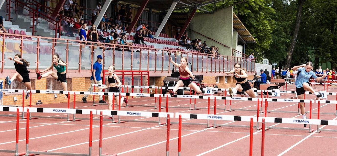 Zawodniczki biegną przez płotki na stadionie lekkoatletycznym.