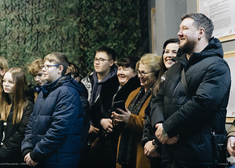 Kilkanaście osób reaguje z uśmiechem na słowa mężczyzny przemawiającego na otwarciu wirtualnej