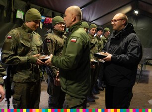 Żołnierz i mężczyzna w cywilnym ubraniu wręczają paczki żołnierzom