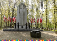 Pomnik z flagami, przed nim stoją żołnierze