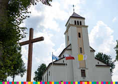 Drewniany krzyż i trzy flagi na tle kremowego kościoła