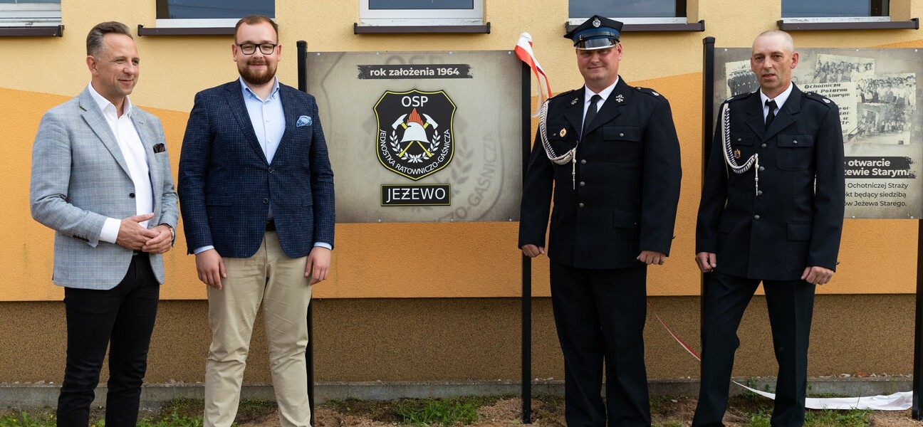 Wicemarszałek Łukaszewicz i burmistrz Choroszczy oraz dwóch strażaków w mundurach stoją przy tablicach na budynku