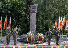 Pomnik Żołnierzy Armii Krajowej, przy nim leżą wieńce, po obu stronach stoją żołnierze 