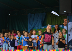 Dzieci zebrane na scenie, biorą udział w konkursie rzucania papierowymi samolotami