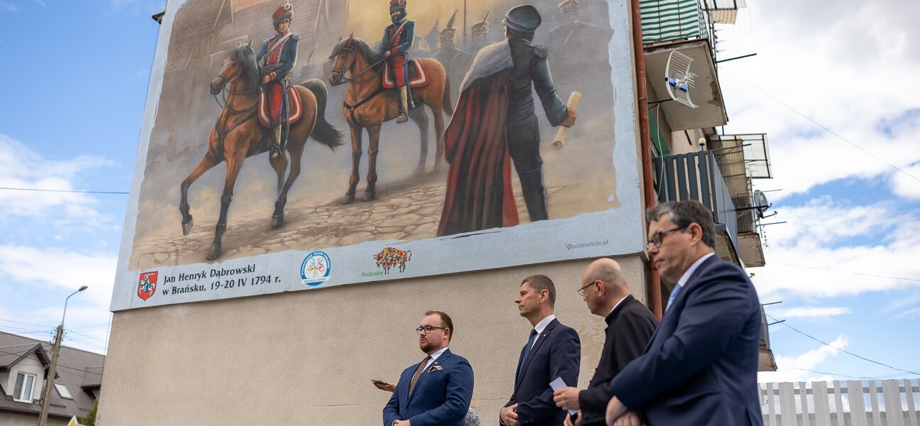 Czterech mężczyzn po prawej stronie. Po lewej budynek z muralem.