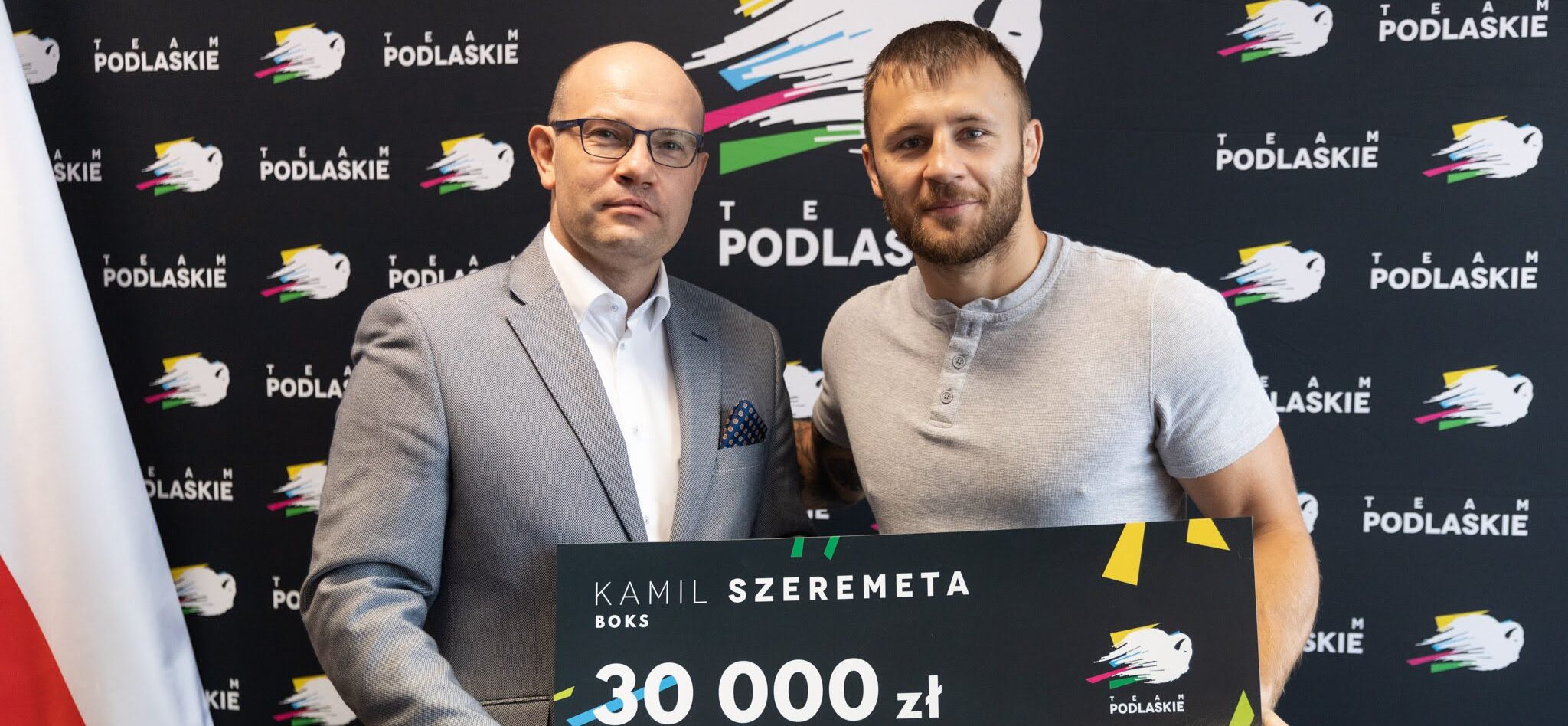 Artur Kosicki i Kamil Szeremeta pozują, prezentując symboliczny czek.