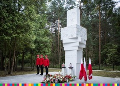 Biały pomnik z napisem: Ofiarom faszyzmu. Po lewej stronie trzej chłopcy, po prawej flagi
