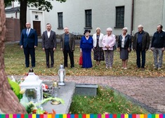 Osoby stoją z kwiatami i zniczami przed grobem ks. Suchowolca