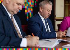 Dwóch mężczyzn podpisuje dokumenty na tle logo województwa podlaskiego