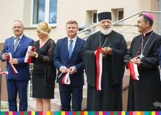 Marek Malinowski trzyma w dłoni przeciętą biało-czerwoną szarfę i stoi obok osób duchownych