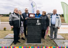 Kilka osób stoi przy obelisku. Jeden z mężczyzn trzyma grawerton