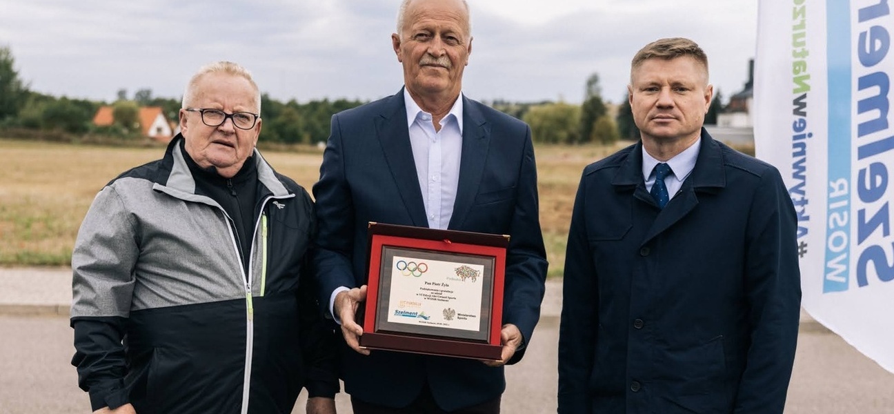 Trzej mężczyźni stoją obok siebie. Jeden z nich trzyma pamiątkowy grawerton