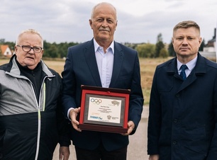 Trzej mężczyźni stoją obok siebie. Jeden z nich trzyma pamiątkowy grawerton